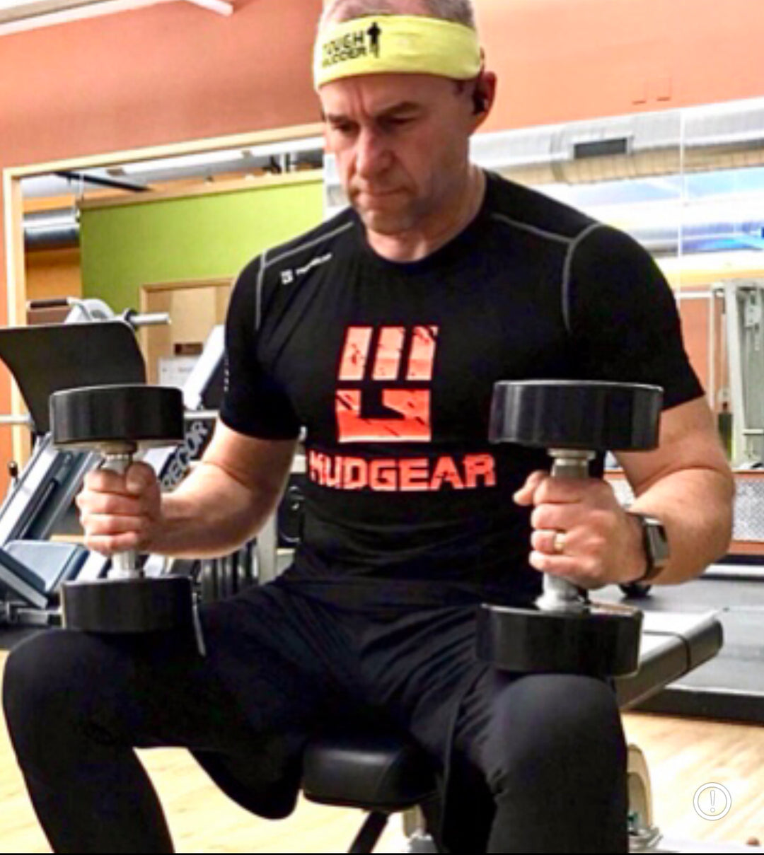 Dave Didier lifts some weights in an indoor gym sporting a MudGear performance shirt. 